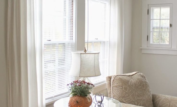 Уютный уголок в гостиной с белыми шторами, креслом и столиком у окна.